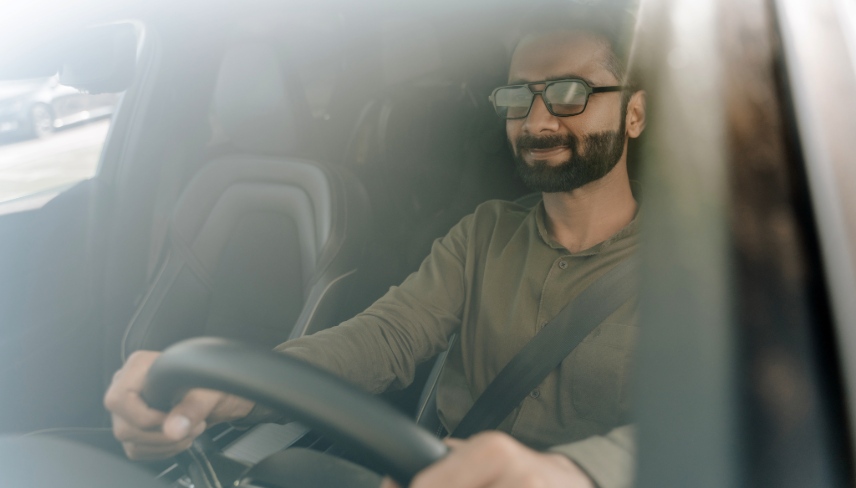 Confident businessman driving a car on a sunny day. Looking relaxed and happy. Wearing sunglasses.