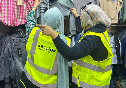 Two women in headscarves and Intertek branded worker vests browse children's clothing