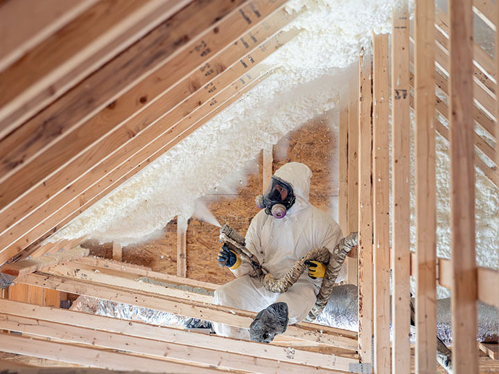 Construction worker in white hazmat suit spraying insulation in attic of home
