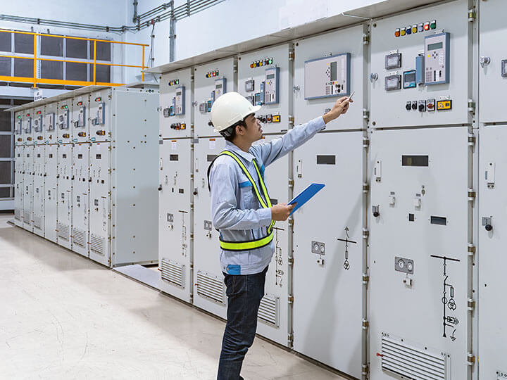 Young industrial engineer with tablet checking the switch panels of switchgear room of an energy power plant