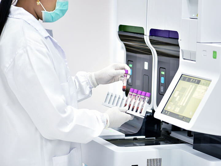 Female medical technologist in white coat and protective mask using diagnostic tools for blood samples
