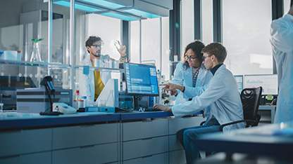 Un groupe de professionnels en blouse de laboratoire effectuant des tests analytiques et examinant les données sur des ordinateurs dans un laboratoire. 