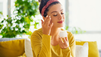  A woman applies cream to her face, focusing on skincare and self-care routines.