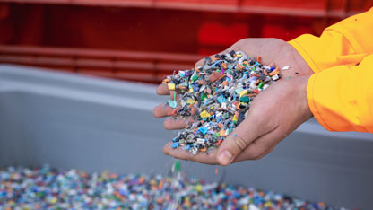 Open hands holding a scoop of loose plastic resin pellets