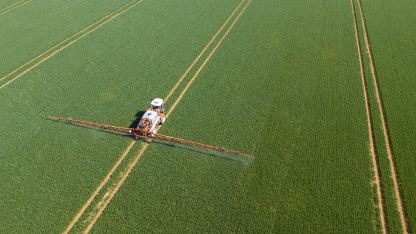 Aerial view of a tractor applying spray to a large agricultural field, showcasing farming practices from above.