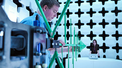 Engineers checking a bilog antenna for electromagnetic compatibility (EMC) radiated immunity testing in a semi anechoic chamber relative to the electronic equipment under test